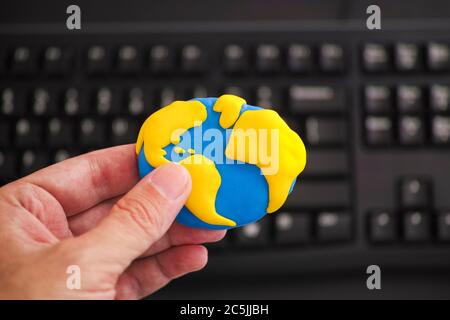 Homme tenant la planète Terre dans sa main au-dessus d'un clavier d'ordinateur noir. La planète Terre est faite d'argile polymère. Banque D'Images