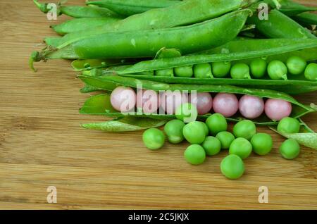 Surprise dans une gousse, perles roses et pois verts sur une surface en bois Banque D'Images