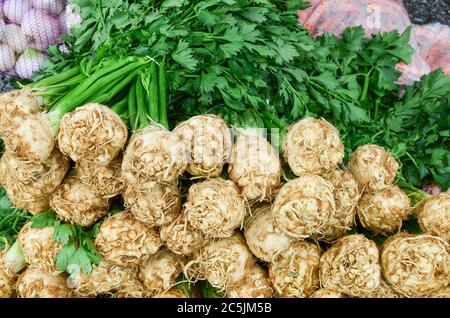 Céleri, racine et feuilles frais et entiers sur le marché de gros, avec un peu d'oignon et de carottes en arrière-plan Banque D'Images