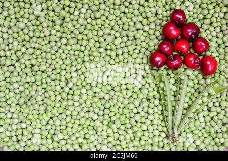 Arrière-plan de cerises et de pois, forme de fleur faite de cerises fraîches et mûres et de gousses de pois sur des pois décortiqués Banque D'Images