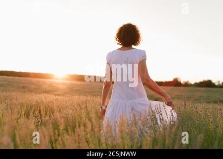 Belle femme dans une robe blanche marche dans le champ de lavande contre le soleil se tord au coucher du soleil Banque D'Images