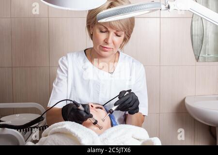 L'esthéticienne effectue la procédure de micro-courant dans le salon de beauté. La procédure stimule la production de collagène, le levage, combat les rides, le visage Banque D'Images