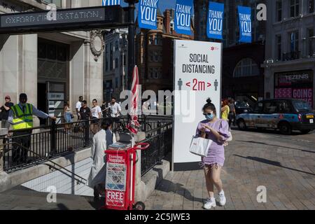 184 autres personnes ont déclaré avoir été victimes de Covid au Royaume-Uni au cours des 24 dernières heures, soit un total de 43,414, une cabas frotte du gel désinfectant dans ses mains en passant par Oxford Circus où un poste conseille aux Londoniens d'observer les distances sociales correctes de deux mètres, pendant le confinement de la pandémie de Covid, Maintenant, après trois mois de la politique de séjour à la maison, mais maintenant, étant détendu comme les magasins rouvrent, le 26 juin 2020, à Londres, en Angleterre. Les restrictions gouvernementales sur la règle des 2 mètres seront reappliquées le 4 juillet et remplacées par « un mètre plus » dans l'espoir qu'elle stimule l'économie britannique en difficulté. Banque D'Images