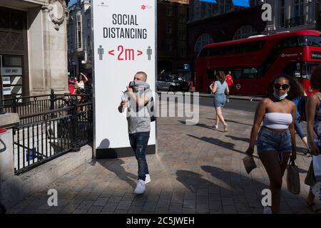 Avec 184 autres décès signalés au Royaume-Uni au cours des 24 dernières heures, soit un total de 43,414, les acheteurs passent par Oxford Circus où un poste conseille aux Londoniens d'observer les distances sociales correctes de deux mètres, pendant le confinement de la pandémie de Covid, Maintenant, après trois mois de la politique de séjour à la maison, mais maintenant, étant détendu comme les magasins rouvrent, le 26 juin 2020, à Londres, en Angleterre. Les restrictions gouvernementales sur la règle des 2 mètres seront reappliquées le 4 juillet et remplacées par « un mètre plus » dans l'espoir qu'elle stimule l'économie britannique en difficulté. Banque D'Images