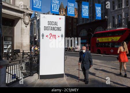 Avec 184 autres décès signalés au Royaume-Uni au cours des 24 dernières heures, soit un total de 43,414, les acheteurs passent par Oxford Circus où un poste conseille aux Londoniens d'observer les distances sociales correctes de deux mètres, pendant le confinement de la pandémie de Covid, Maintenant, après trois mois de la politique de séjour à la maison, mais maintenant, étant détendu comme les magasins rouvrent, le 26 juin 2020, à Londres, en Angleterre. Les restrictions gouvernementales sur la règle des 2 mètres seront reappliquées le 4 juillet et remplacées par « un mètre plus » dans l'espoir qu'elle stimule l'économie britannique en difficulté. Banque D'Images