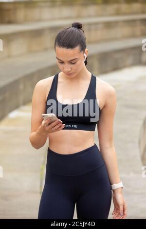 Une femme sportive vêtue de vêtements de sport et portant un téléphone portable Banque D'Images