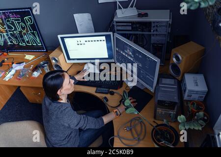 Femme est très occupée avec son travail à l'ordinateur dans le programme d'édition vidéo. Une femme est assise sur une chaise à la table dans photo Studio. Concept de travail informatique. Lipik Banque D'Images