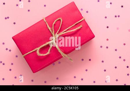 Boîte cadeau rose attachée avec ficelle sur un fond rose clair orné de petites étoiles étincelantes. Concept de vacances. Pose à plat. Vue de dessus. Copier l'espace Banque D'Images