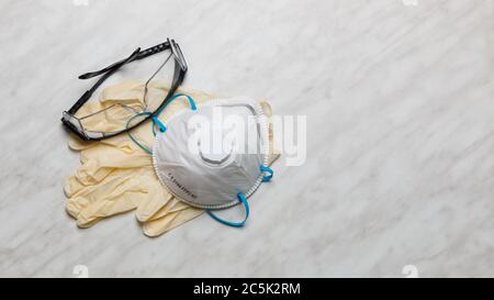 Masque blanc FFP2, N95 avec lunettes et gants en latex sur une table blanche, vue du dessus. Banque D'Images