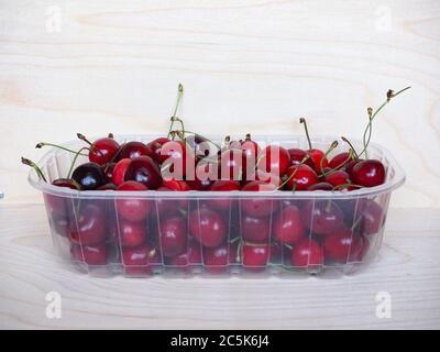 cerises rouges dans un panier en plastique sur une table en bois Banque D'Images