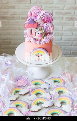 Gâteau d'anniversaire rose avec licorne, nuages arc-en-ciel et nuages meringues. Bar à bonbons avec gâteau, biscuits et sucettes. Banque D'Images