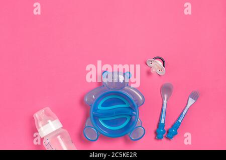 Assiette bleue sous forme d'ours, bouteille, couteau et cuillère sur table rose. Repas des enfants. Vue de dessus Banque D'Images