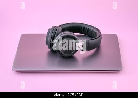Ordinateur portable en métal et casque noir sur fond rose. Ordinateur portable fermé avec écouteurs. Le concept de l'auto-éducation Banque D'Images
