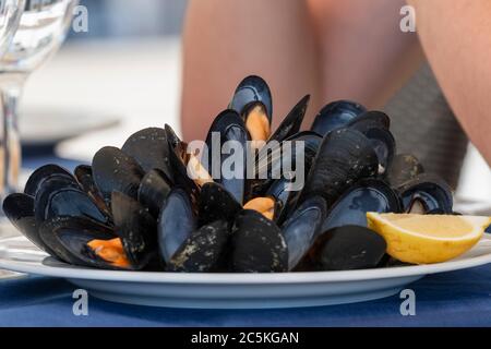 Gros plan de moules cuites appétissantes avec une tranche de citron sur une assiette blanche sur une table sur un fond défocaliste. Concept de nourriture saine et de vacances. Banque D'Images