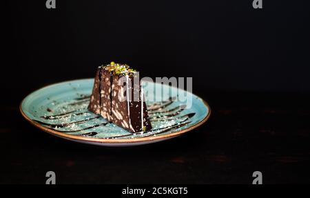 un gâteau en mosaïque sur une assiette de couleur, fond noir, avec sauce au chocolat Banque D'Images