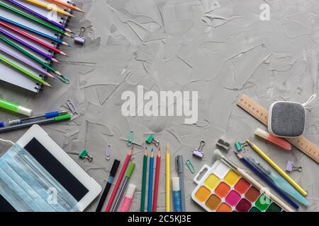 Les fournitures scolaires bordent le fond en béton gris avec un masque médical. Concept de cadre de rentrée. Nouvelle normalité, auto-éducation sur l'auto-isolement. Banque D'Images