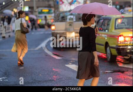 Femme avec parapluie traversant la route dans la rue Shibuya pendant une nuit de pluie, Tokyo, Japon Banque D'Images