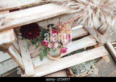 Fleurs rouges et roses dans un vase en verre posé sur des planches en bois. Décoration rustique. Banque D'Images