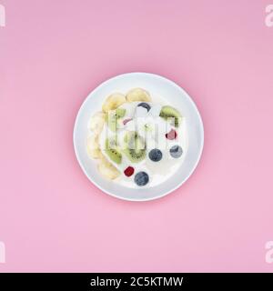 Un bol de smoothies aux superaliments : yaourt, bleuets, kiwi, amandes, banane, noix. Vue de dessus sur fond rose. Banque D'Images