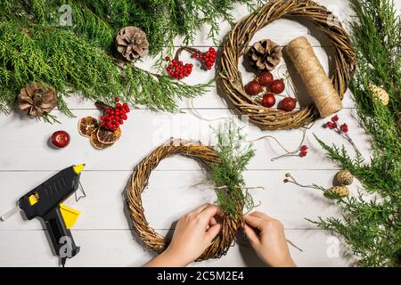 Fond de Noël fait main. Fabrication de couronne et de décorations de Noël artisanales. Vue de dessus de la table en bois blanc avec les mains des femmes. Banque D'Images