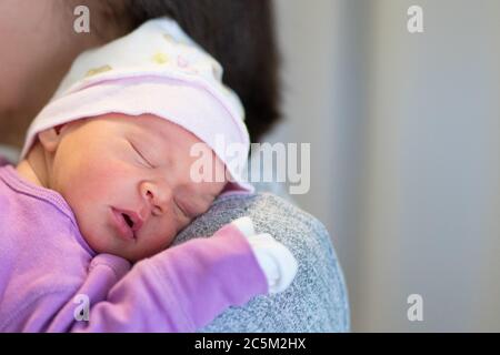 Maman tient sa petite fille d'un mois sur l'épaule pendant qu'elle dort. Banque D'Images