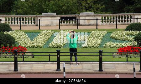 Londres, Royaume-Uni. 03ème juillet 2020. Un touriste prend une photo des parterres de fleurs.deux parterres de fleurs spéciales de 30 pieds de long ont été dévoilées devant le palais de Buckingham en hommage aux travailleurs du NHS avant le 72e anniversaire du Service de santé. Les parterres de fleurs colorées, qui étaient bien plus que NHS, ont été plantés aux jardins du Mémorial, dans le parc St James. Crédit : SOPA Images Limited/Alamy Live News Banque D'Images