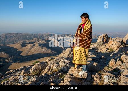 Un kurde enveloppé dans une couverture se dresse au sommet du parc national du Mont Nemrut en Turquie au lever du soleil. Banque D'Images