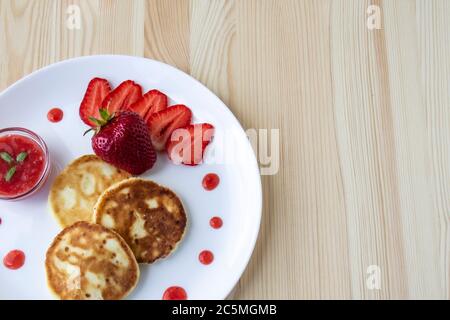 Trois crêpes au fromage et aux fraises et sauce sur un plat blanc sur fond de bois. Délicieux fromage pancake et fraises pour la pause Banque D'Images