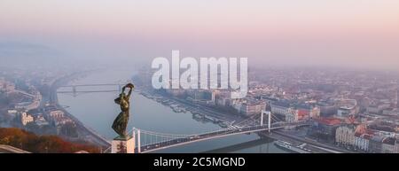 Vue aérienne de la Statue de la liberté avec le pont Elisabeth et le Danube, prise de la colline Gellert au lever du soleil dans le brouillard à Budapest, Hongrie. Banque D'Images