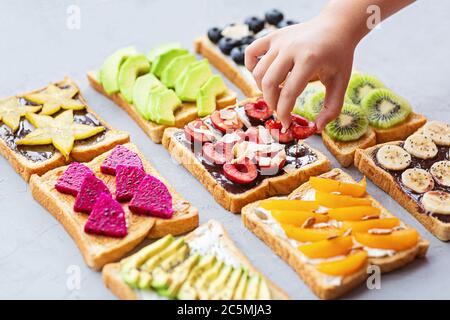 Sandwiches au fromage à la crème, au chocolat, aux fruits frais et aux baies (avocat, bleuets, bananes, kiwi, cerise, abricot, fruit dragon) sur un fond gris Banque D'Images