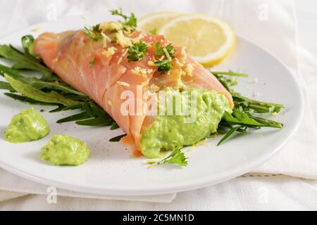 Rouleau de saumon rempli de purée de pois sur une salade de roquette avec des tranches de citron et une garniture aux herbes sur une assiette blanche, repas bas de carb, concentration sélectionnée, profondeur étroite de Banque D'Images