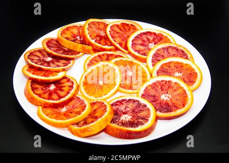 ​​orange en tranches siciliennes sur une plaque blanche sur fond sombre. Tranché des oranges siciliennes mûres sur fond. ​​orange en tranches rouges sain et savoureux Banque D'Images