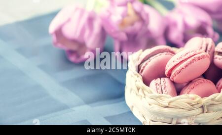 Des macarons traditionnels français multicolores sont rangées dans un panier sur le fond d'un bouquet de fleurs. Gros plan, mise au point sélective. Copier l'espace Banque D'Images