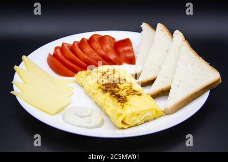 Petit déjeuner incroyable avec omelette savoureuse, tomates, fromage, pain et sauce sur la plaque blanche. Omelette délicieuse faite comme rolle, autres ingrédients. Savoureux Banque D'Images