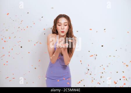 Belle jeune femme asiatique se tenant isolée sur fond blanc, debout sous confetti Banque D'Images