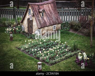 Russie, Sotchi 14.03.2020. Une petite maison de conte de fées se dresse sur une pelouse verte avec un parterre de fleurs avec des tulipes basses lanternes et une clôture derrière Banque D'Images