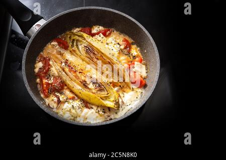 Légumes chicorée frits avec tomates et feta dans une poêle sur un poêle noir, espace de copie, foyer sélectionné, profondeur de champ étroite Banque D'Images