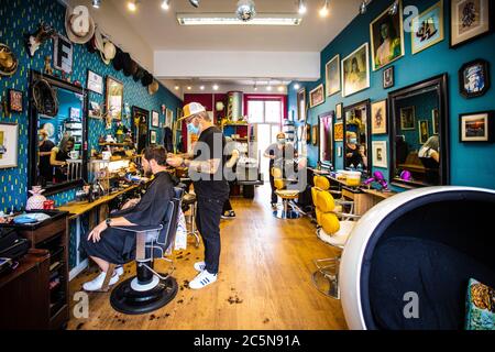 Coiffeur coupant les cheveux en portant un masque facial EPI au salon de coiffure dès les premiers jours de relâchement du verrouillage pendant une pandémie de coronavirus. Angleterre juillet 2020 Banque D'Images