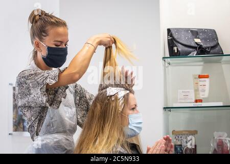 Coiffeur portant un masque facial pendant le travail et coupant les cheveux dans un salon de coiffure comme le blocage du coronavirus facilite en Angleterre 4 juillet 2020 Banque D'Images