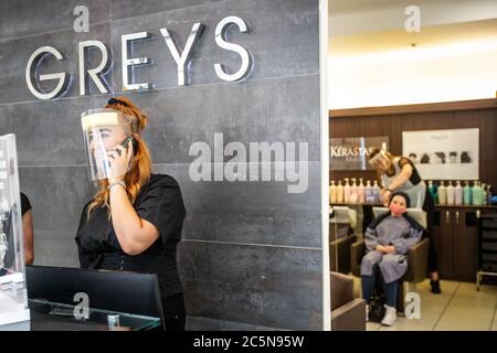 Membre du personnel de l'atelier non essentiel, salon de coiffure portant une visière en EPI, qui accueille les clients et prend des appels téléphoniques pendant la pandémie Covid-19 en Angleterre 2020 Banque D'Images