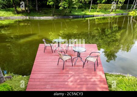 café sur un quai en bois de panneaux rouges avec des tables et des chaises sur la rive de la rivière avec une plante verte, personne. Banque D'Images