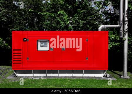 un générateur d'alimentation de secours rouge monté sur une pelouse verte avec arbres verts et un tuyau d'échappement séparé pour la sécurité environnementale. Banque D'Images