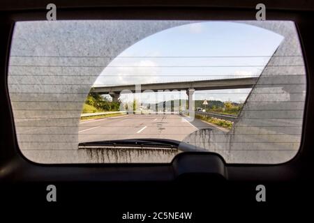 vue de la voiture sale depuis l'intérieur de la voiture par la vitre arrière, la vitre arrière d'une voiture sale avec une vue de la route asphaltée avec des marquages et un pont routier Banque D'Images