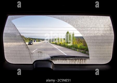 vue de l'intérieur de la voiture par la vitre arrière, la vitre arrière d'une voiture sale avec vue de la route asphaltée avec des marquages et la circulation routière. Banque D'Images