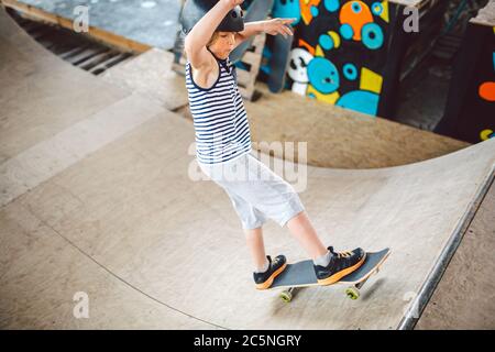 Un skate pour enfants lors de ses tours d'apprentissage sur une rampe dans un parc de skate urbain. Un garçon dans un casque de sport se déplace sur un skate board dans un lieu sportif. Actif Banque D'Images