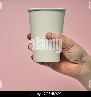 Gobelet en papier à la main sur fond coloré. Matériaux écologiques dans un café, vaisselle jetable biodégradable. Gros plan Banque D'Images