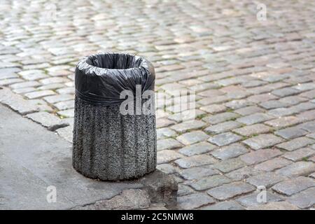 Sac poubelle dans un bac en béton monté sur une chaussée piétonne de pavés avec espace de copie pour le texte. Banque D'Images