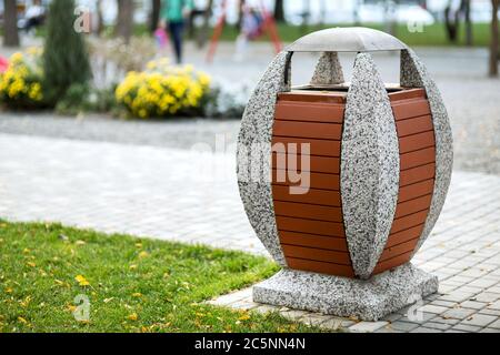 une poubelle ovale sur un stand en béton décoré de planches sur le fond d'un trottoir piétonnier dans une zone du parc. Banque D'Images