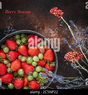 Fraises naturelles fraîches et groseilles à maquereau dans un bol d'eau et des fleurs sur fond sombre Banque D'Images