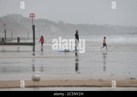 Surfeur sur la plage de Bournemouth malgré la pluie et la bruine que l'on attend dans une grande partie du pays. Banque D'Images